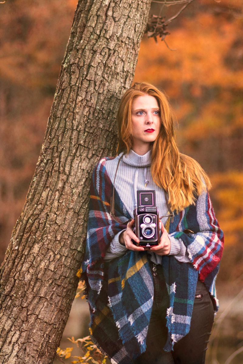 a woman standing next to a tree holding an old camera