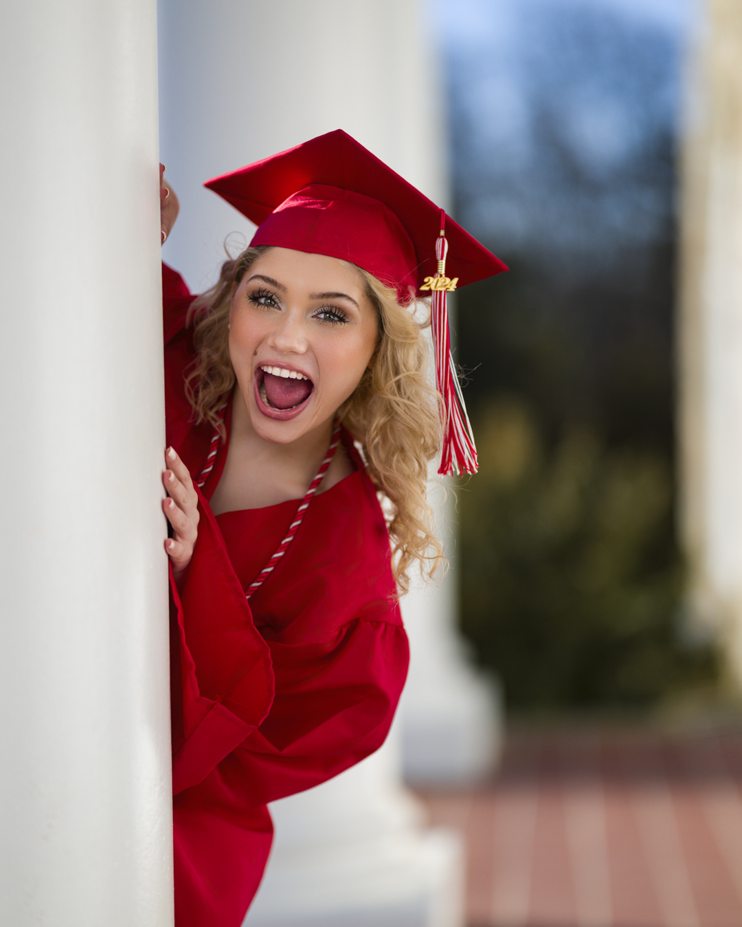 a woman in a red graduation gown is leaning against a column